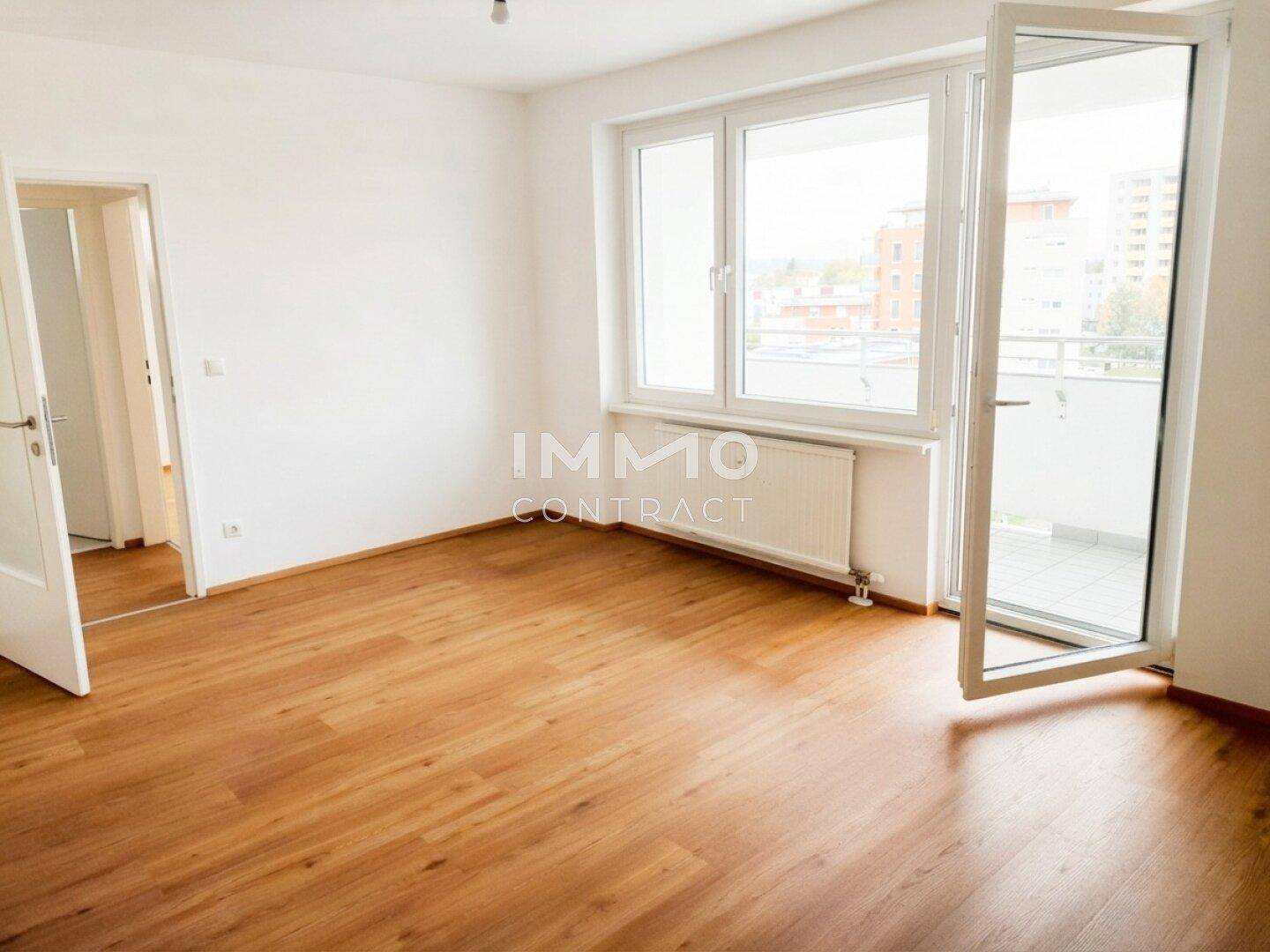 Helles Zimmer mit Holzboden, großem Fenster und Zugang zum Balkon.