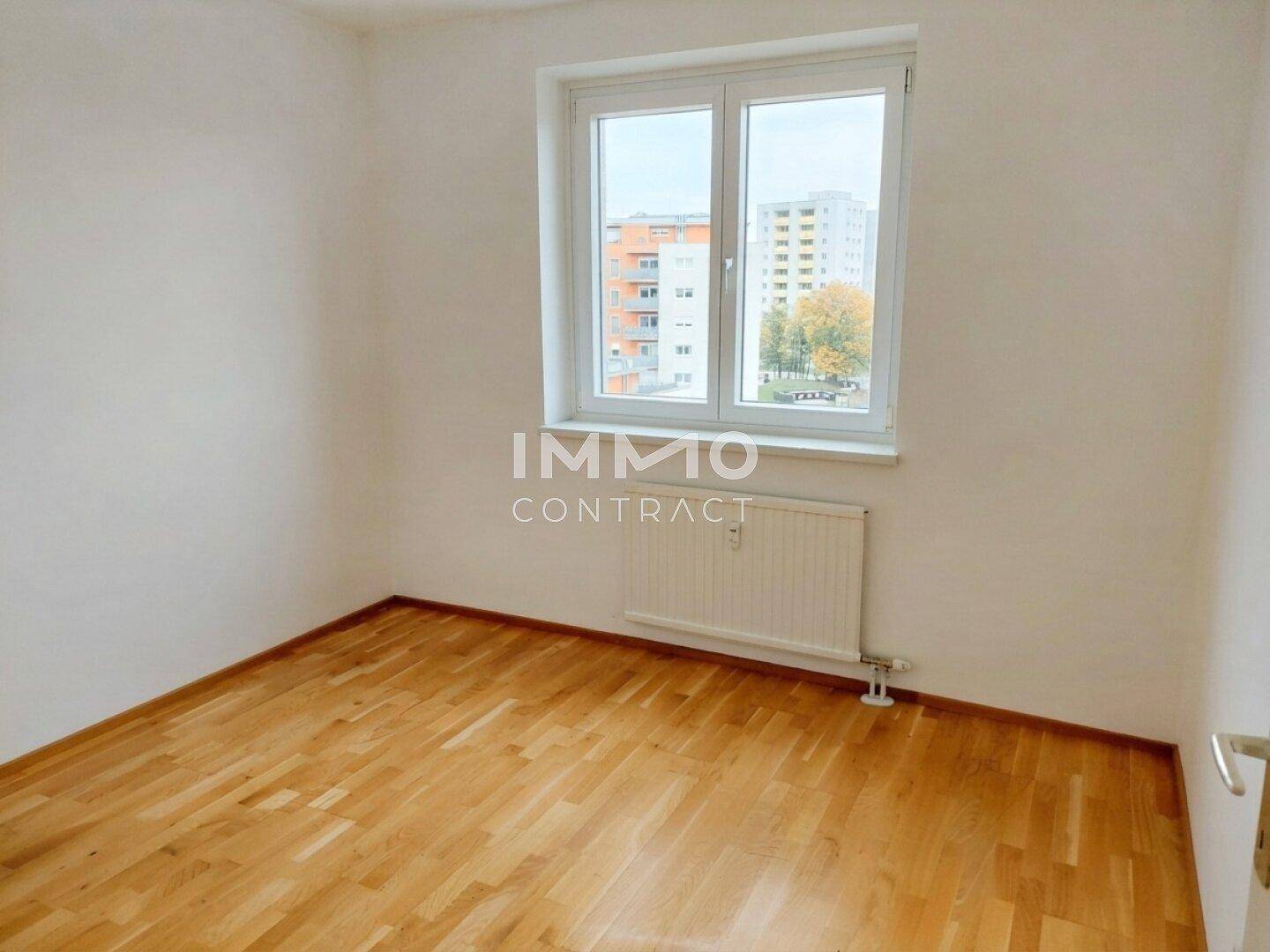 Helles Schlafzimmer mit Parkettboden, großem Fenster und Blick auf die Stadt.