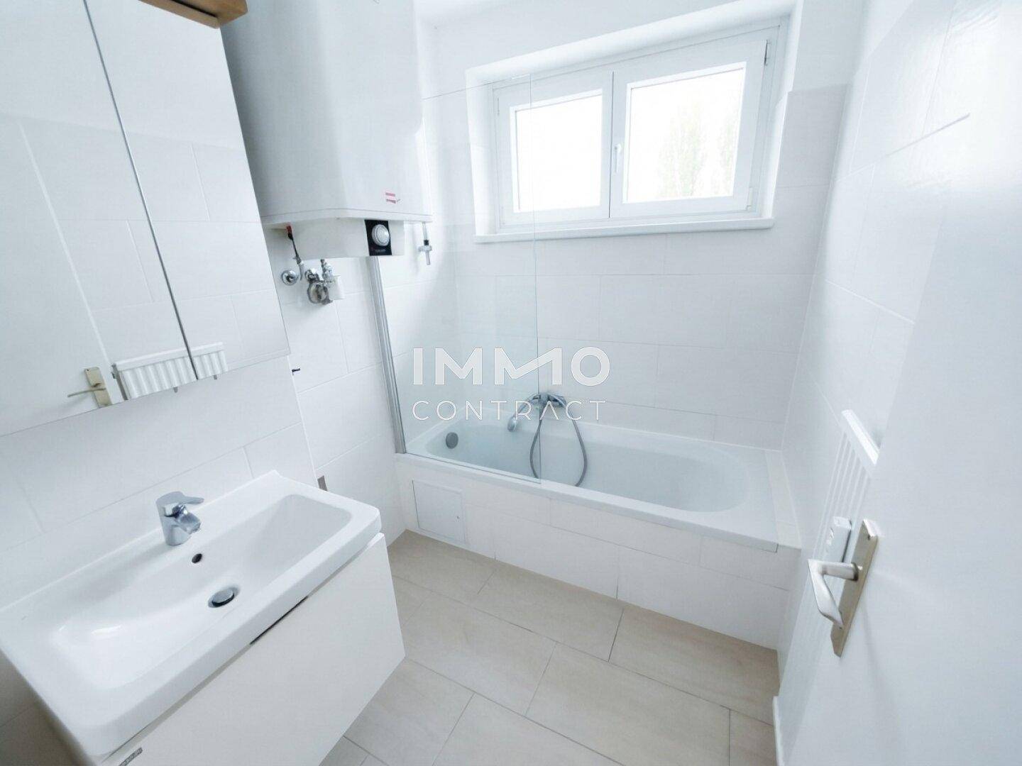 Helles Badezimmer mit Badewanne, Waschbecken und Fenster.
