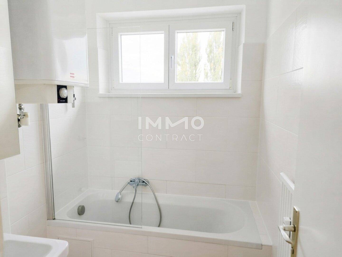 Weiß gefliestes Badezimmer mit Badewanne, Duschvorrichtung und Fenster.