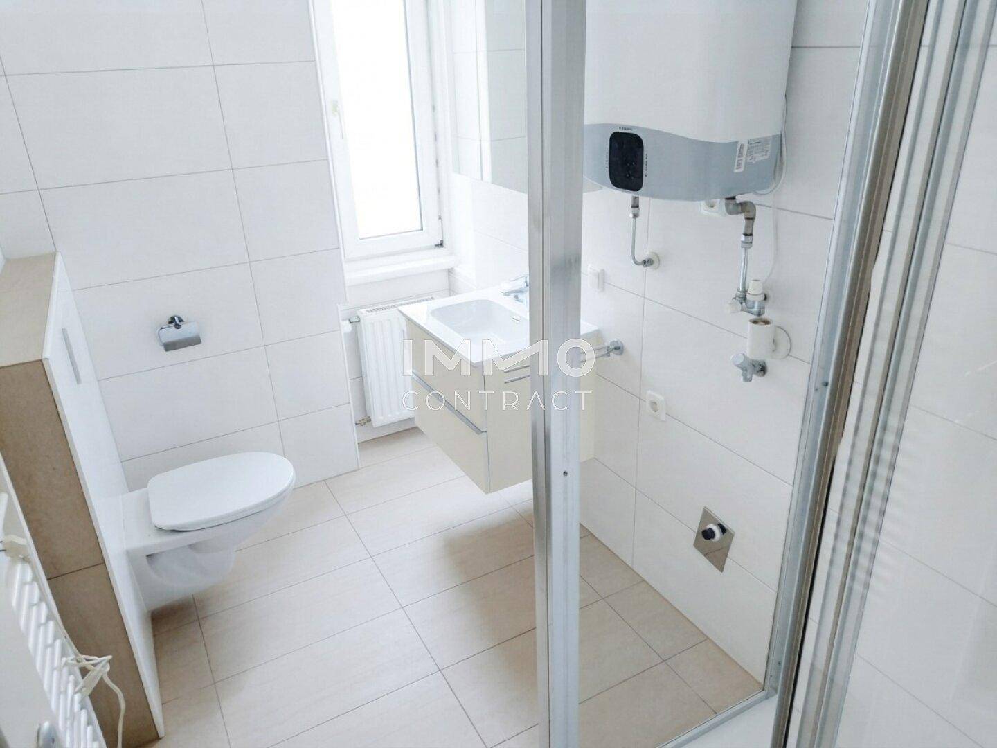 Modernes Badezimmer mit weißen Fliesen, Dusche, WC, Waschbecken und Fenster für Tageslicht.