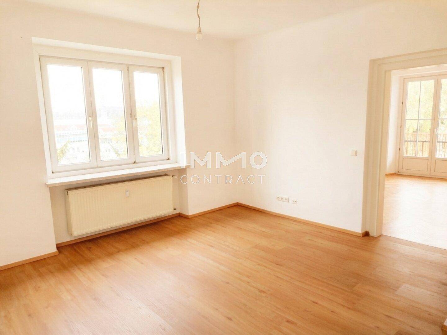 Geräumiges Zimmer mit Parkettboden, großen Fenstern und Heizkörper, ideal als Wohn- oder Schlafzimmer.
