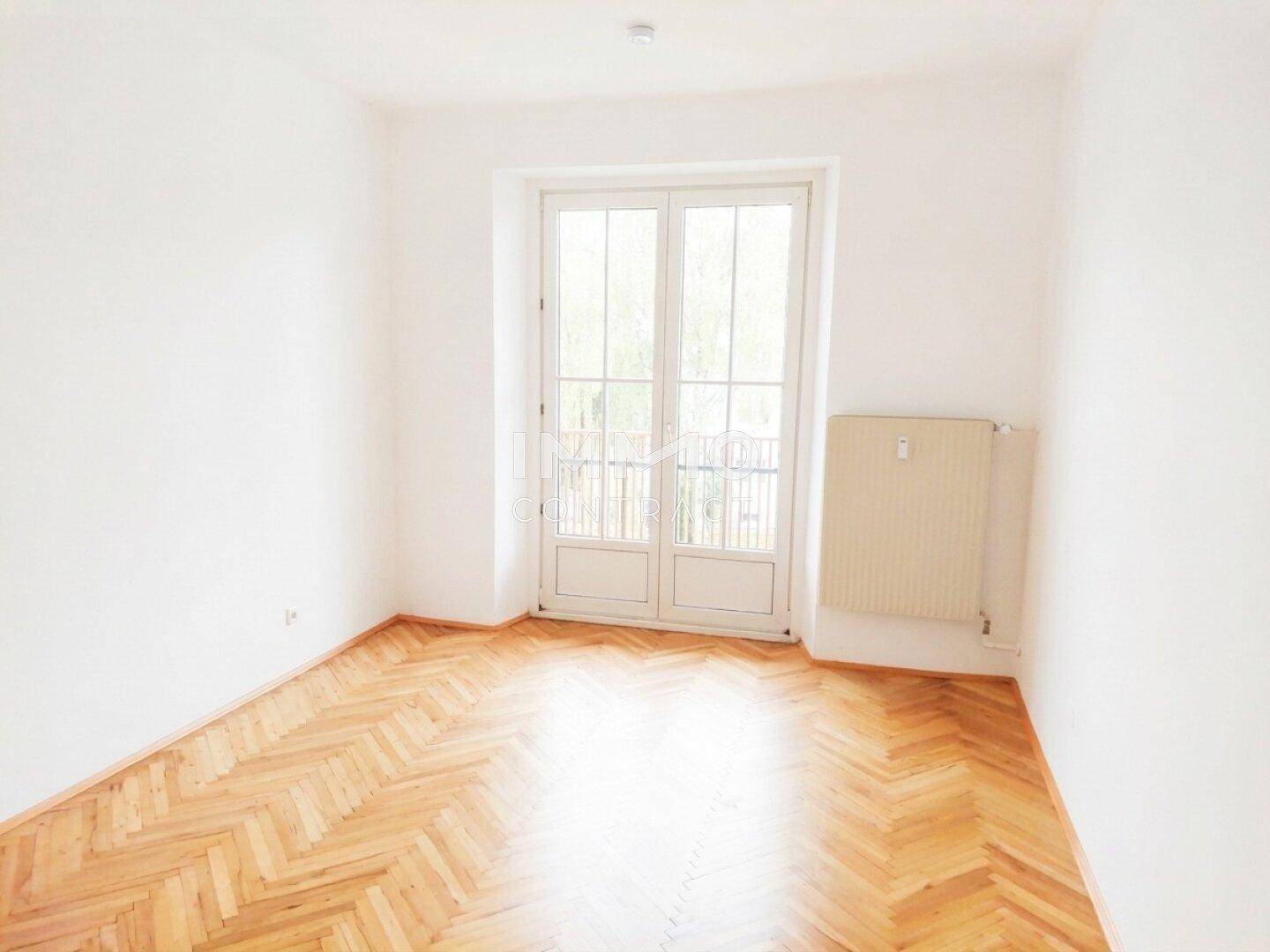 Helles Zimmer mit Fischgrätparkett und Zugang zu einem französischen Balkon, bietet viel Tageslicht.