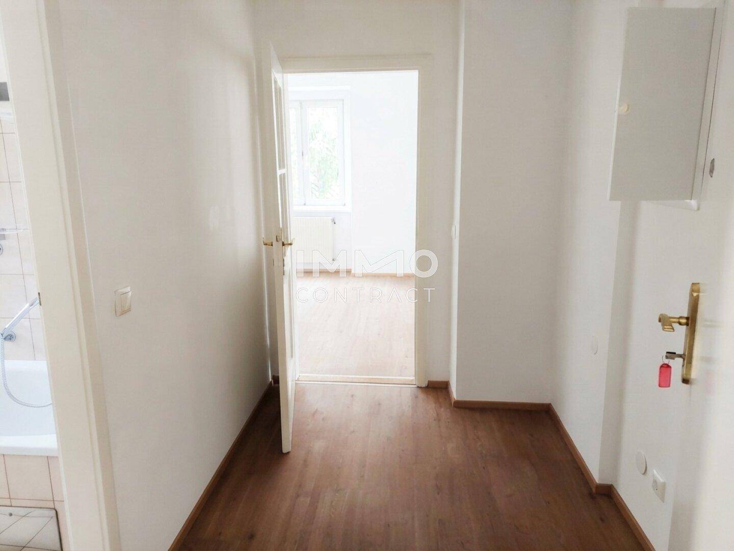 Schmaler Flur mit Holzfußboden, der zu einem weiteren Zimmer und einem Badezimmer führt.