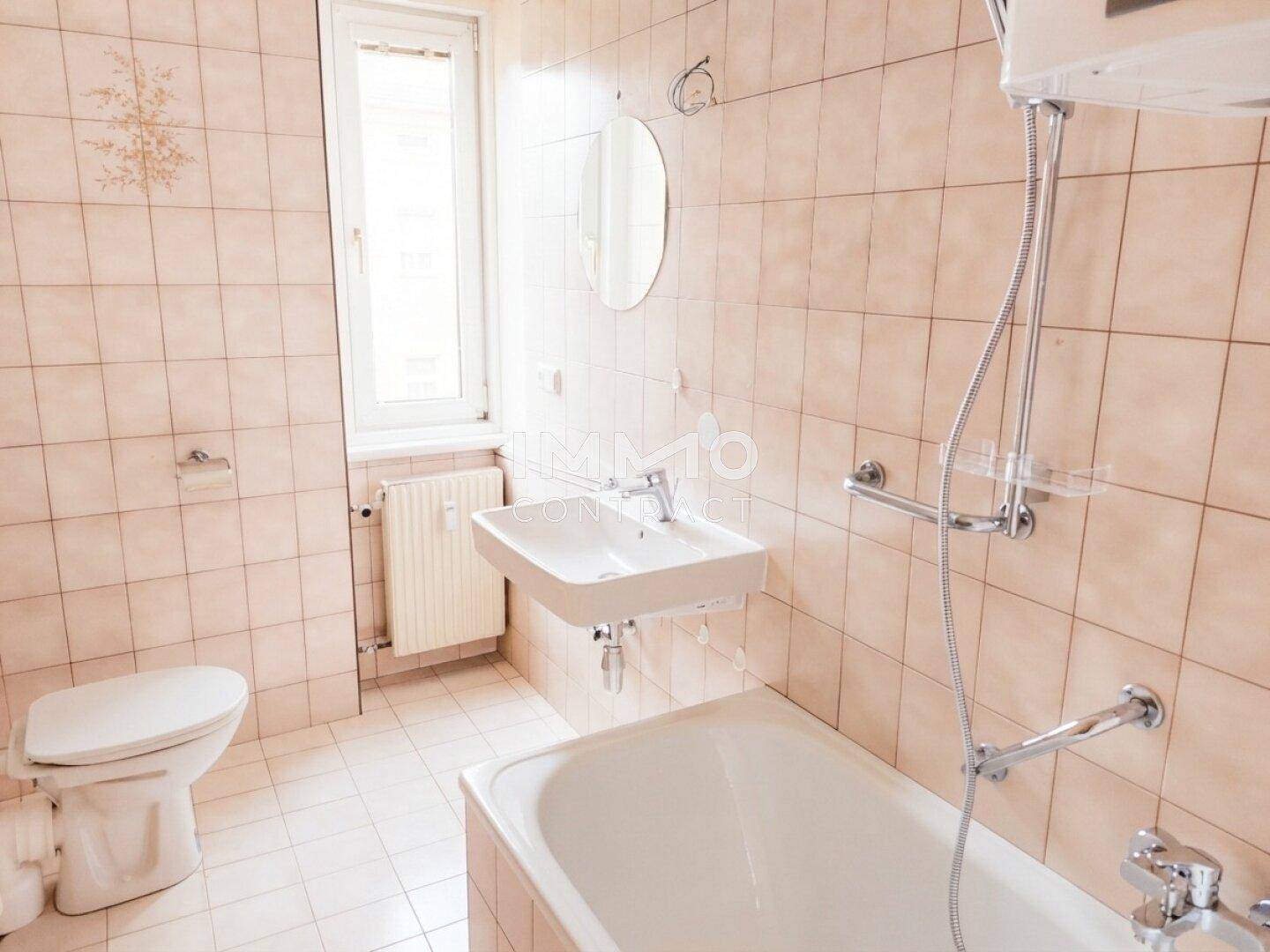 Badezimmer mit beigefarbenen Fliesen, Badewanne, Waschbecken und Fenster für Tageslicht.