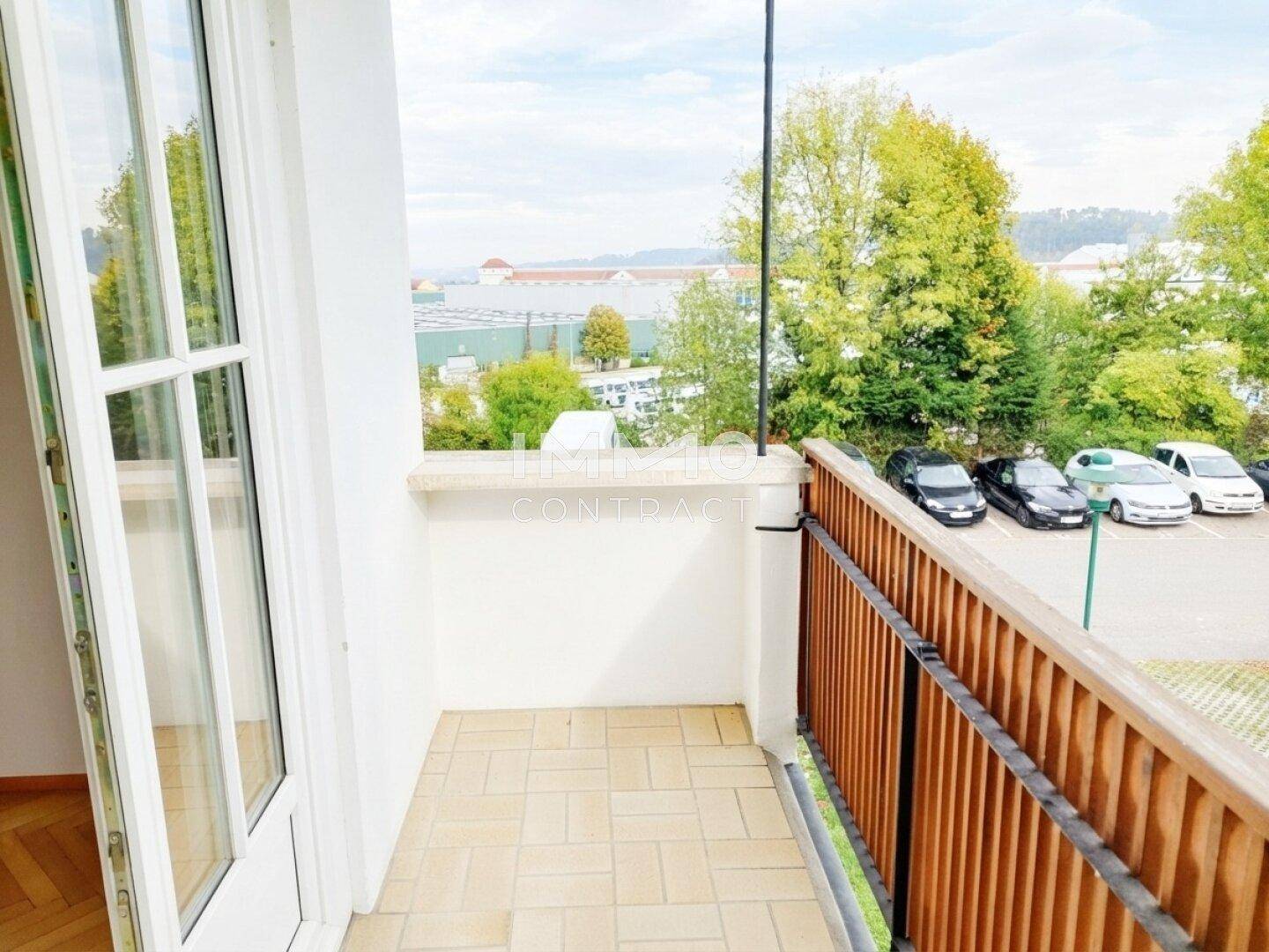 Kleiner Balkon mit Fliesenboden und Blick auf Bäume und einen Parkplatz.