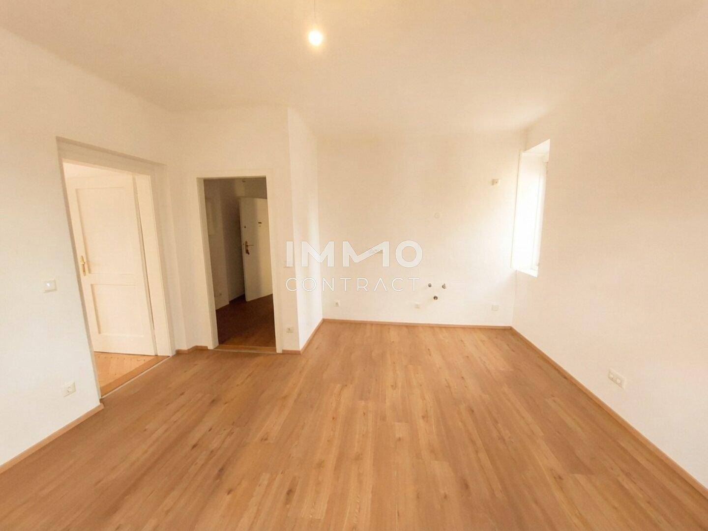 Heller, leerer Raum mit Holzfußboden und Zugang zu weiteren Zimmern.