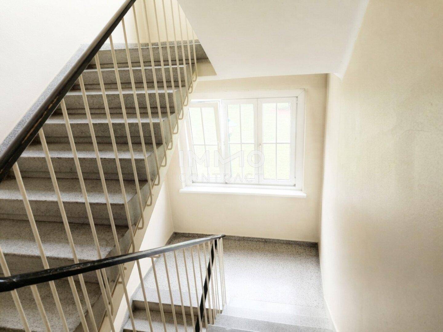 Treppenhaus mit Steinstufen und einem großen Fenster, das den Bereich erhellt.