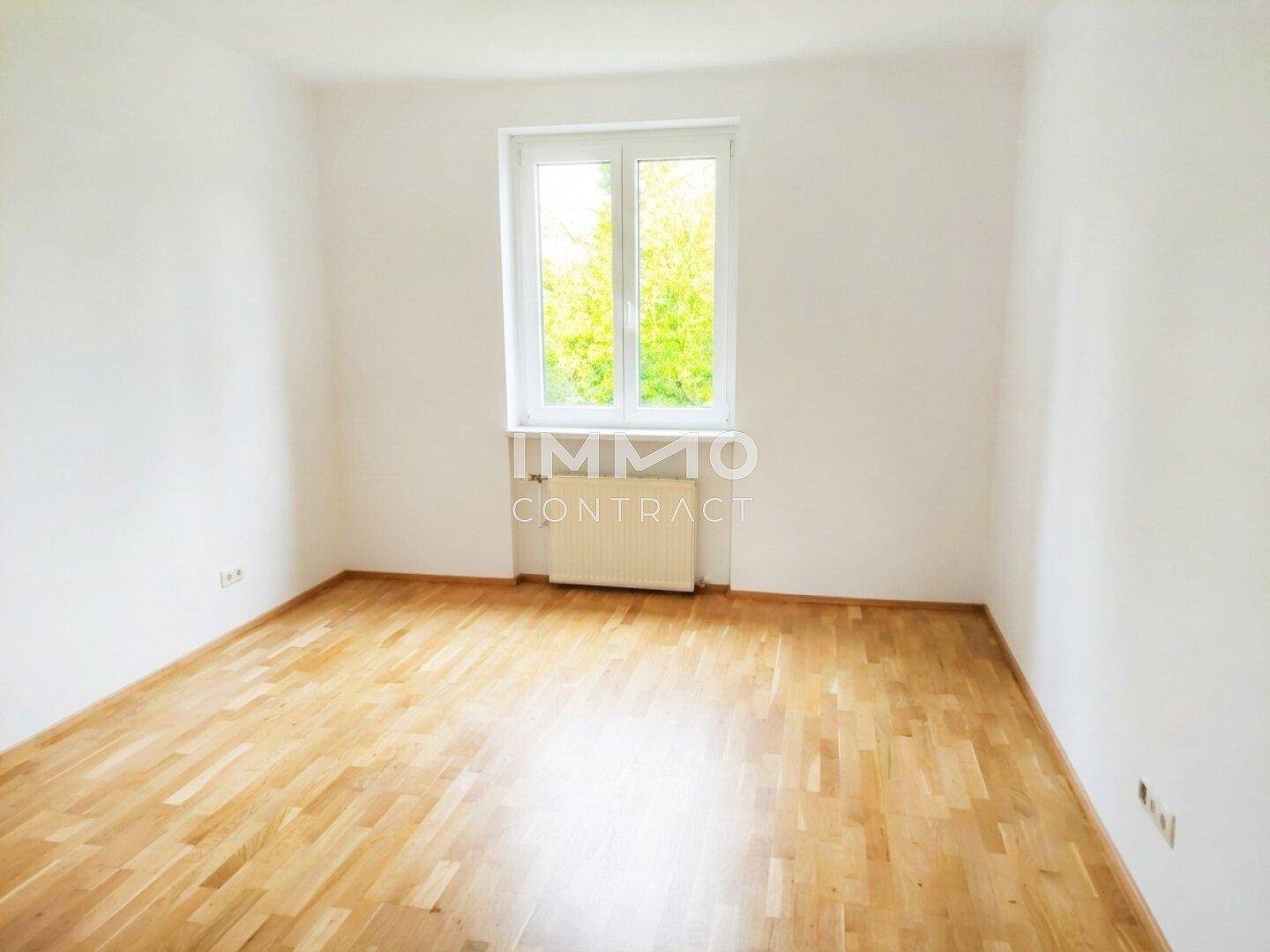 Helles, leeres Zimmer mit Parkettboden und Blick ins Grüne, ideal als Schlaf- oder Arbeitszimmer.