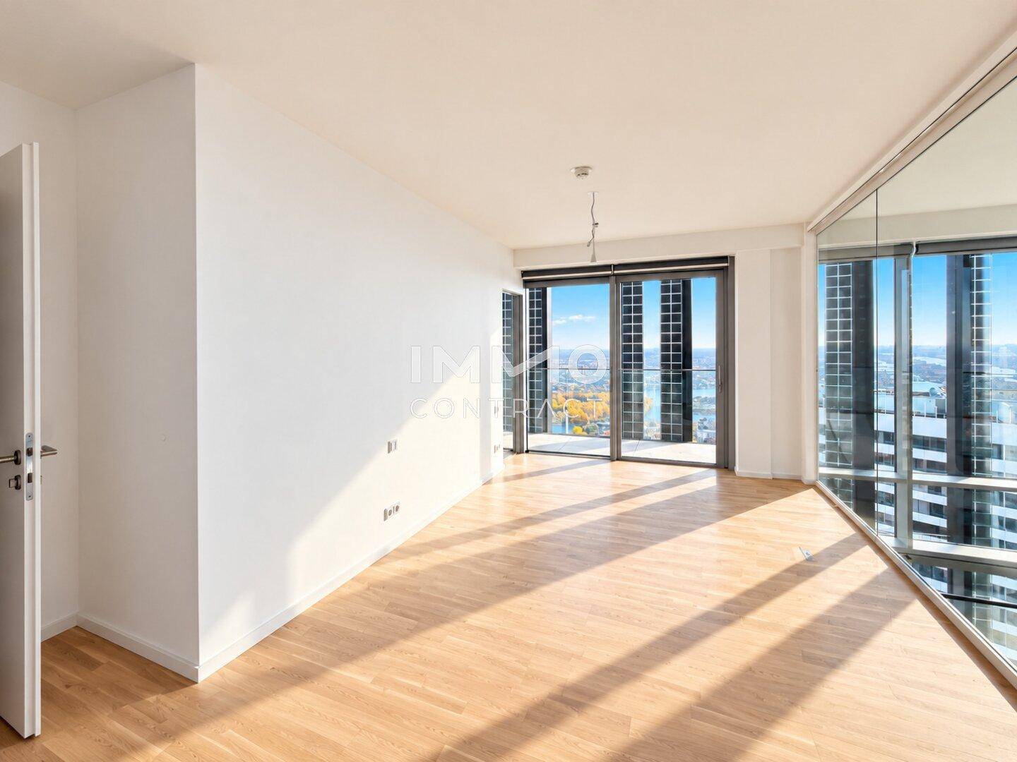 Heller, leerer Raum mit Parkettboden und raumhohen Fenstern, die einen weiten Blick bieten.