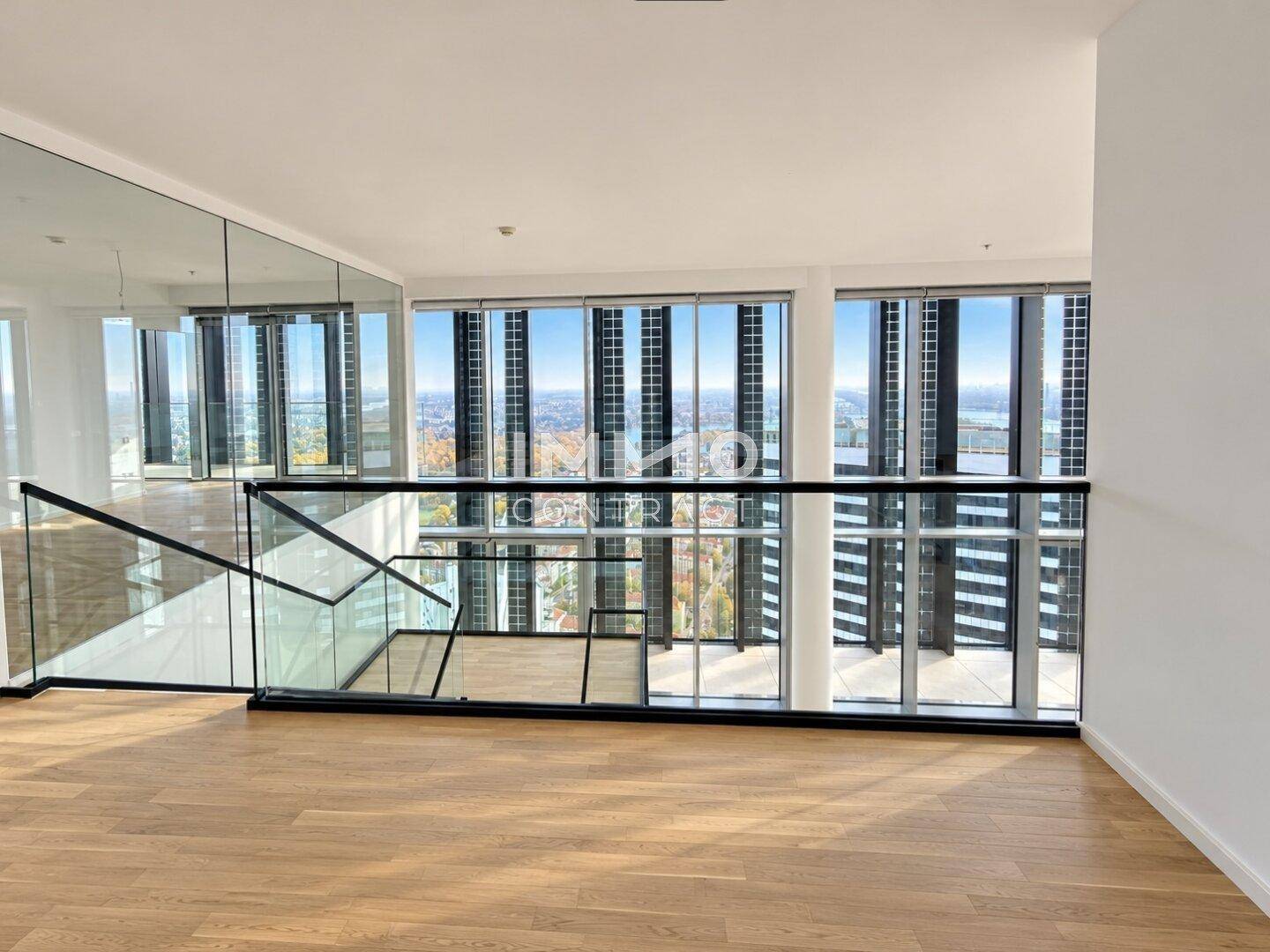 Offener Wohnbereich mit moderner Glasbrüstung und weitem Blick durch die raumhohen Fenster.