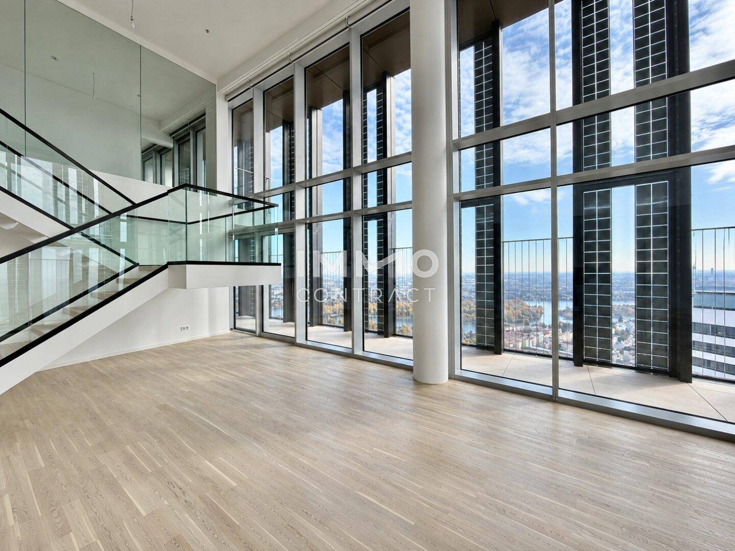 Geräumiger Wohnbereich mit eleganter Treppe, Parkettboden und raumhohen Fenstern mit Panoramablick.