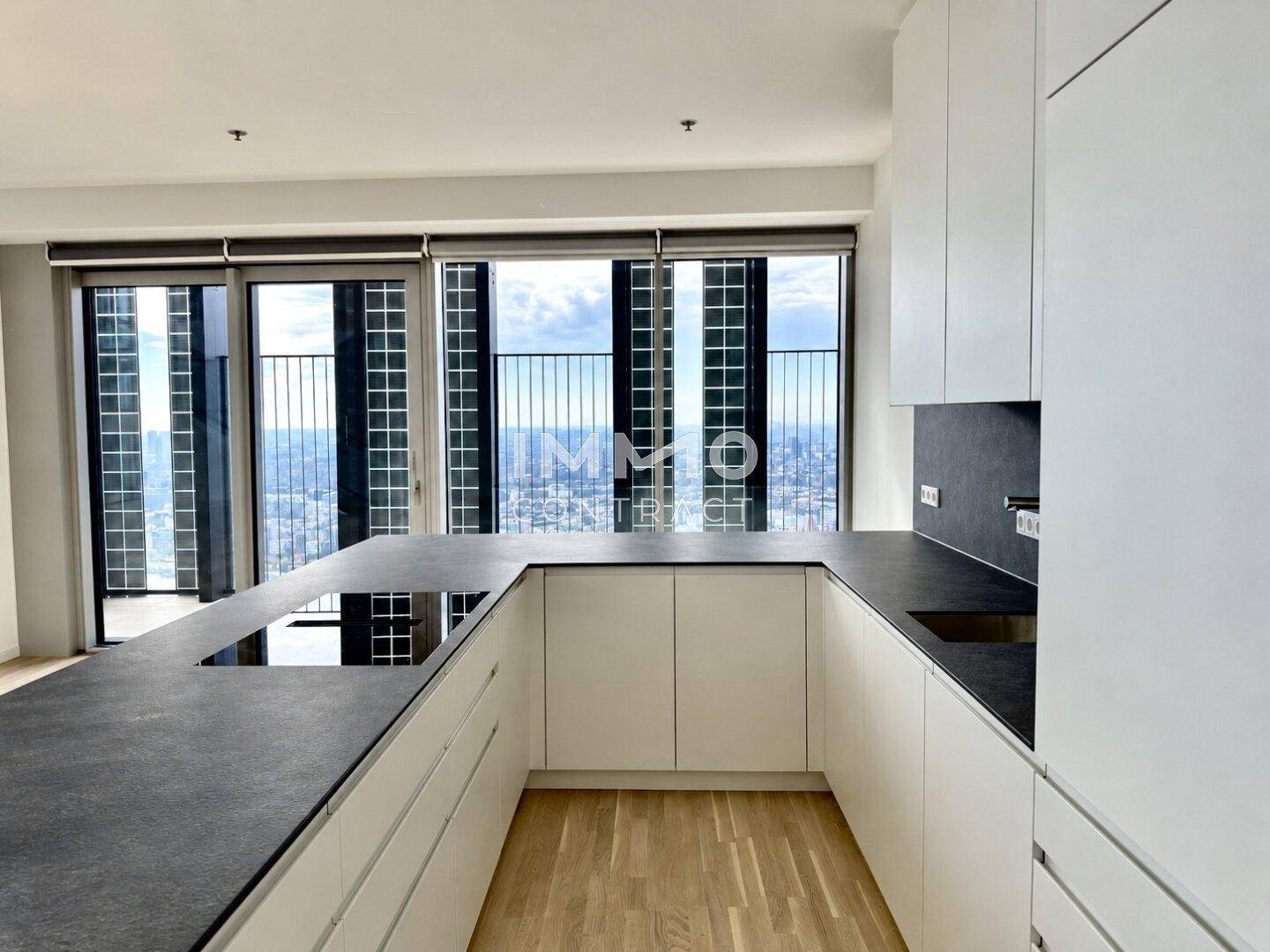 Moderne Küche mit weißen Schränken, dunkler Arbeitsplatte und Induktionskochfeld, bietet Stadtblick.