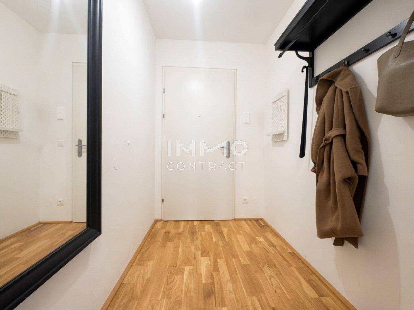 Eingangsbereich mit großem Spiegel, Garderobe und heller Holztür, die zum Inneren führt.