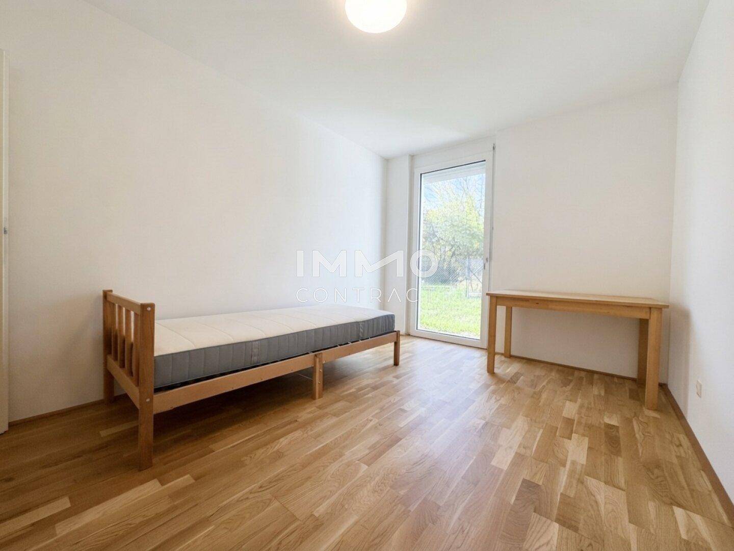 Helles Schlafzimmer mit Einzelbett, Holzboden und großem Fenster mit Blick ins Grüne.