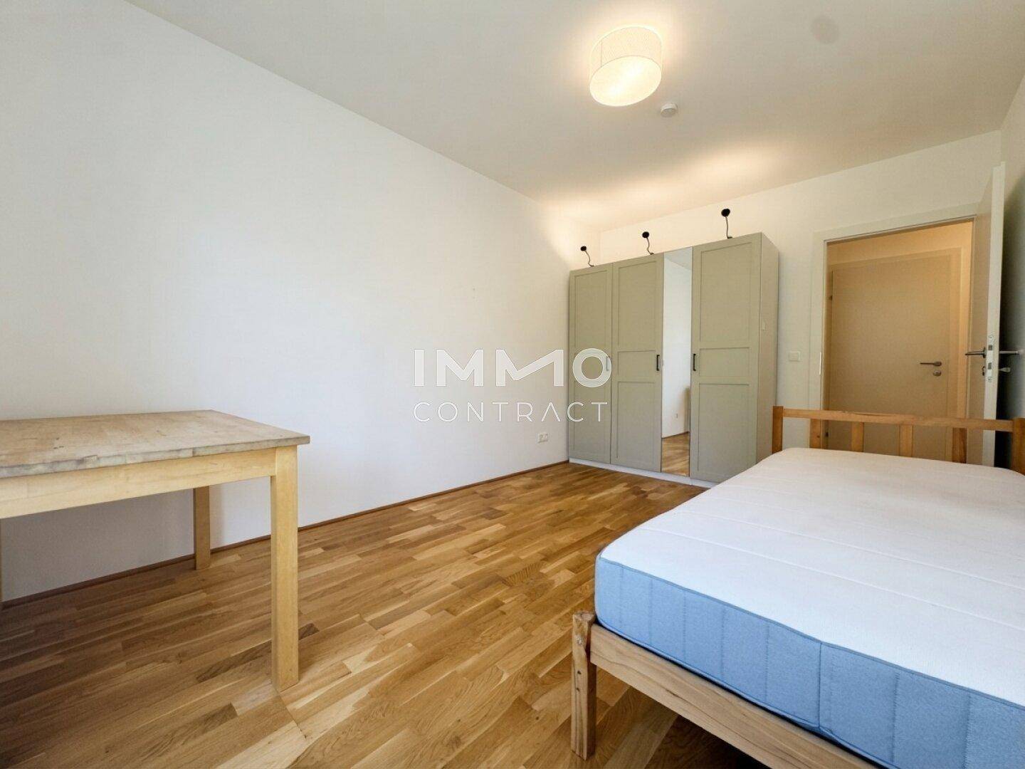 Schlafzimmer mit Holzbett, Schrank und Schreibtisch, ausgestattet mit Parkettboden und hellen Wänden.