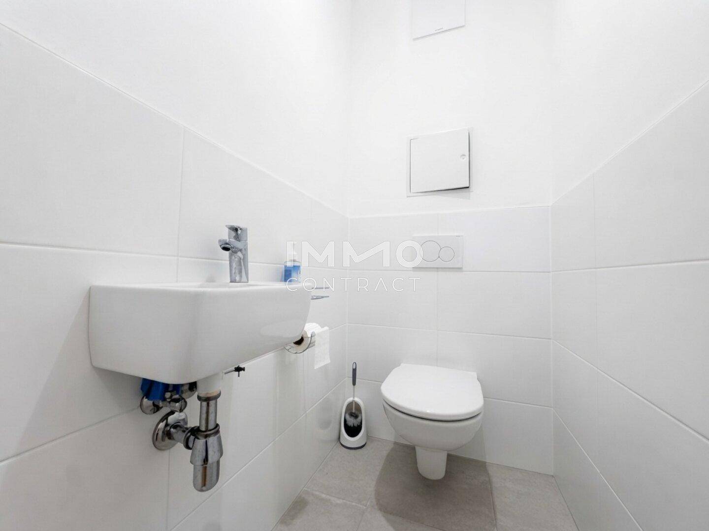 Kleines Gäste-WC mit wandmontierter Toilette und Waschbecken, komplett gefliest in Weiß.