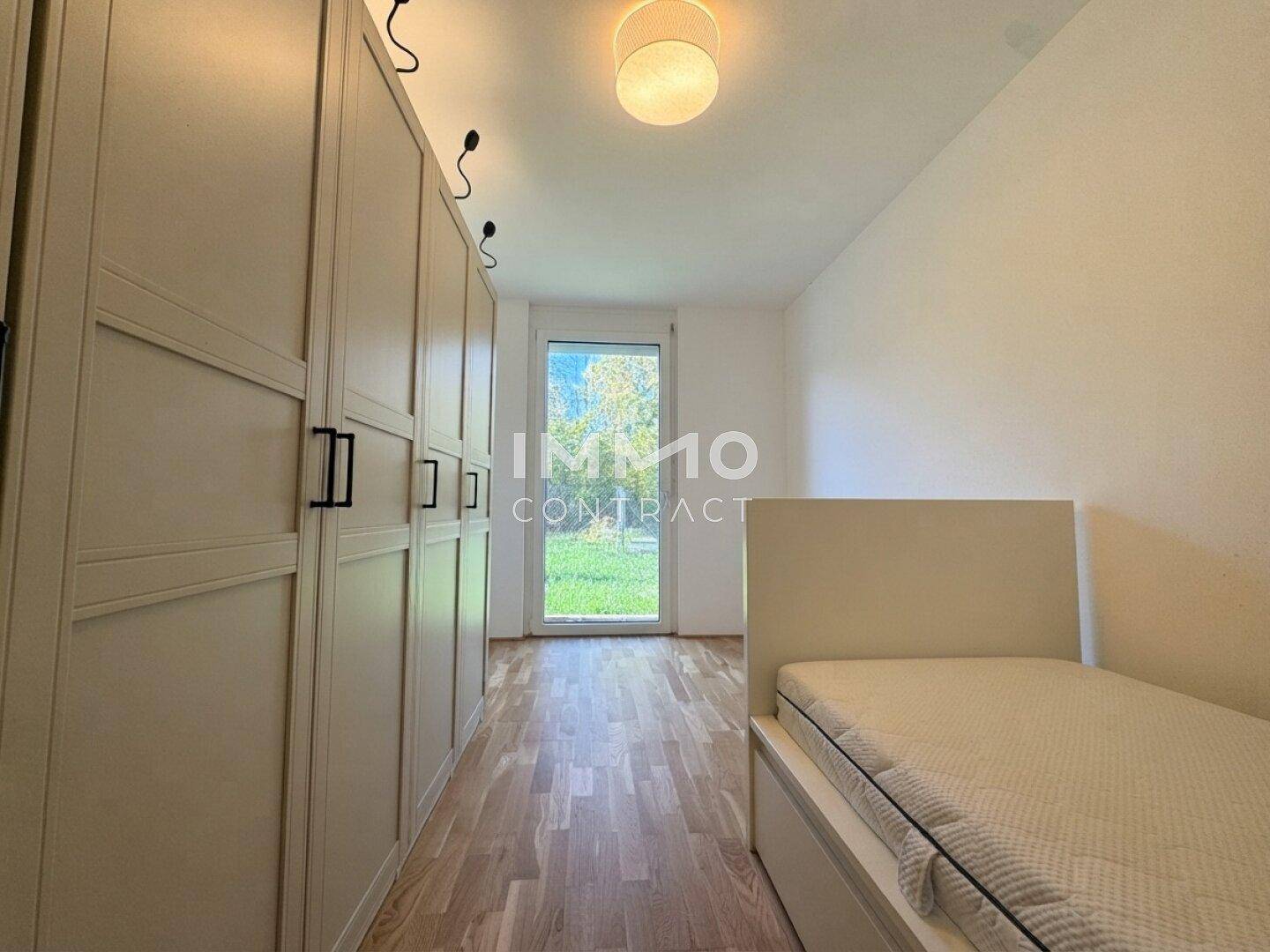 Schlafzimmer mit Einzelbett, großem Kleiderschrank und Zugang zu einem grünen Außenbereich.