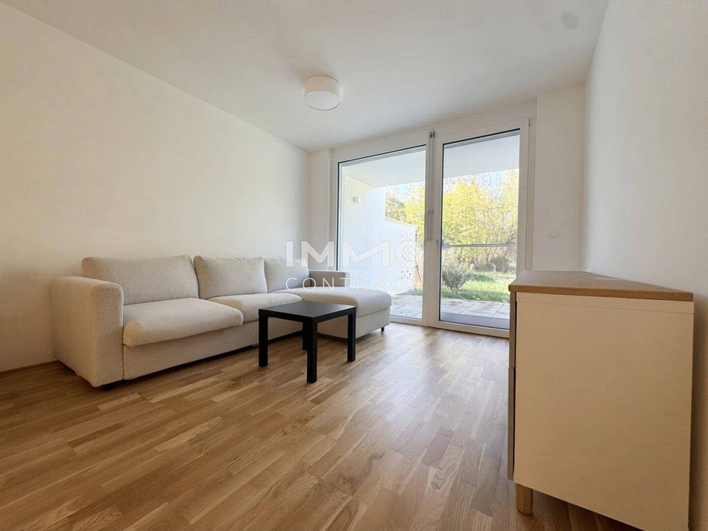 Helles Wohnzimmer mit Parkettboden, gemütlichem Sofa und großem Fenster mit Zugang zum Außenbereich.
