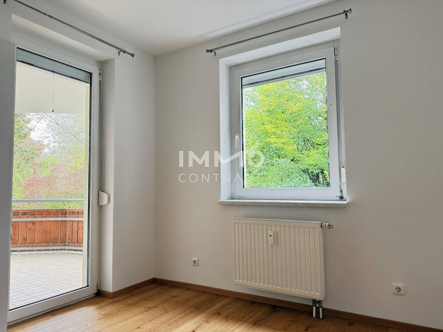 Helles Schlafzimmer mit Holzboden, Fenster und Zugang zu einem Außenbereich.
