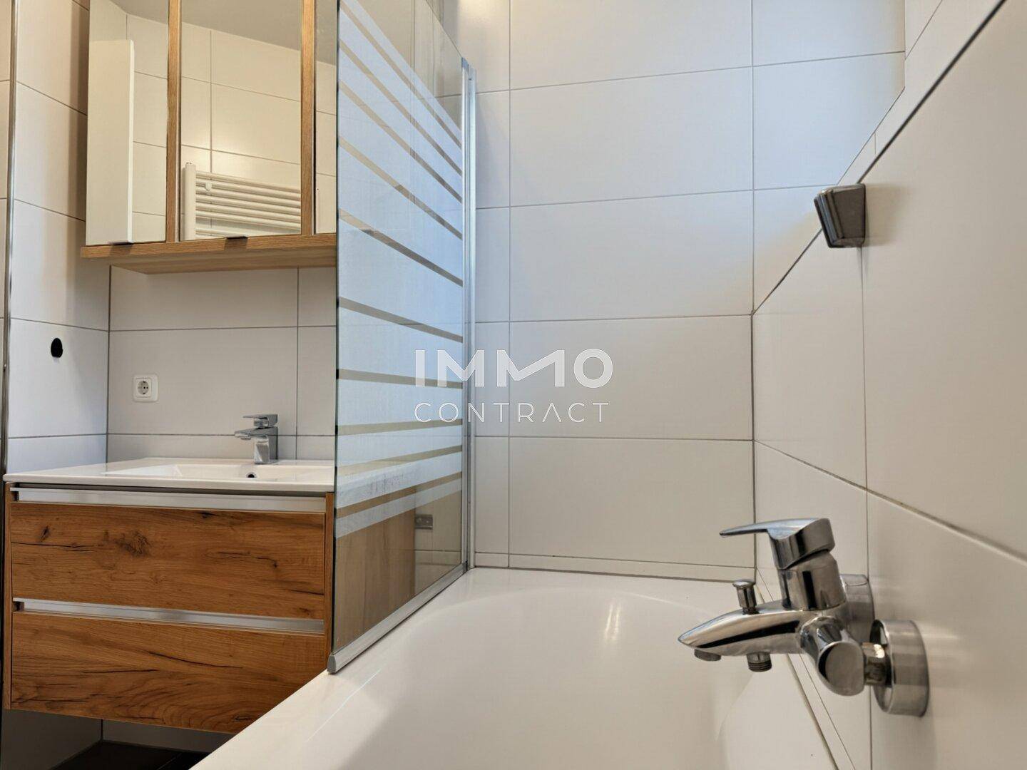 Modernes Badezimmer mit Badewanne, Waschbecken und Spiegelschrank, hell gefliest.
