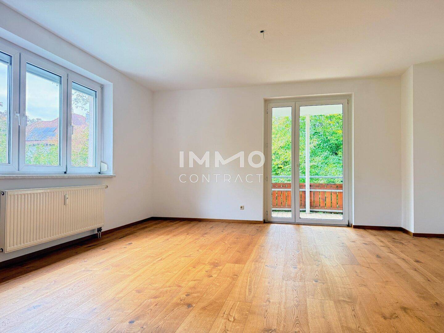 Geräumiges Wohnzimmer mit Holzboden, großen Fenstern und direktem Zugang zum Balkon.