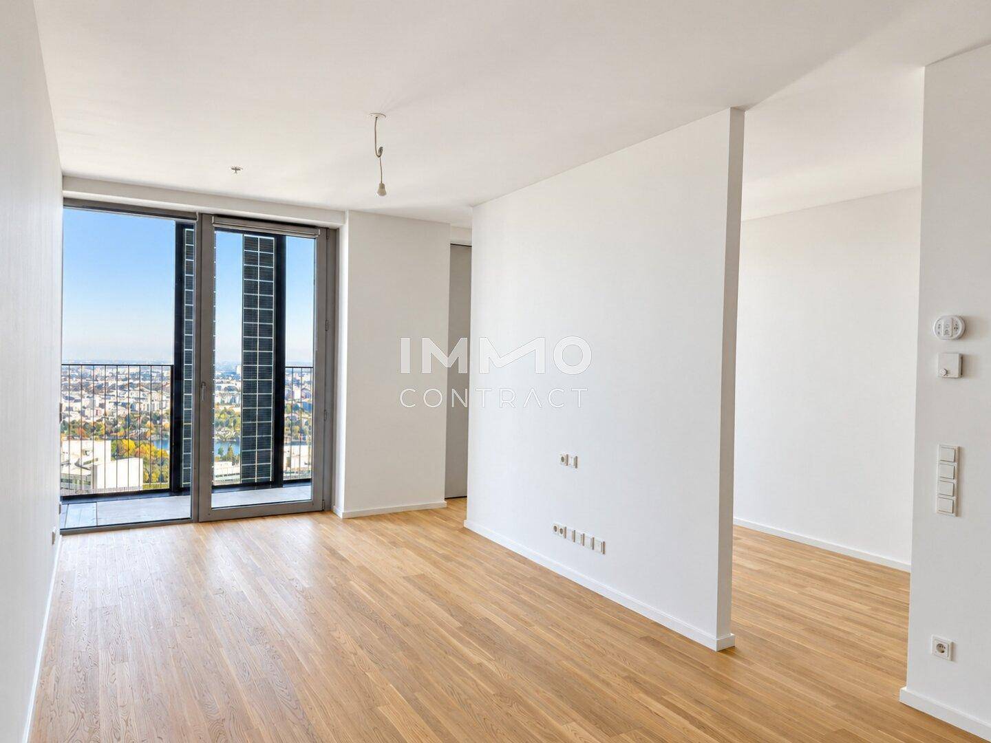 Heller, leerer Wohnbereich mit Parkettboden und Zugang zu einem Balkon mit Stadtblick.