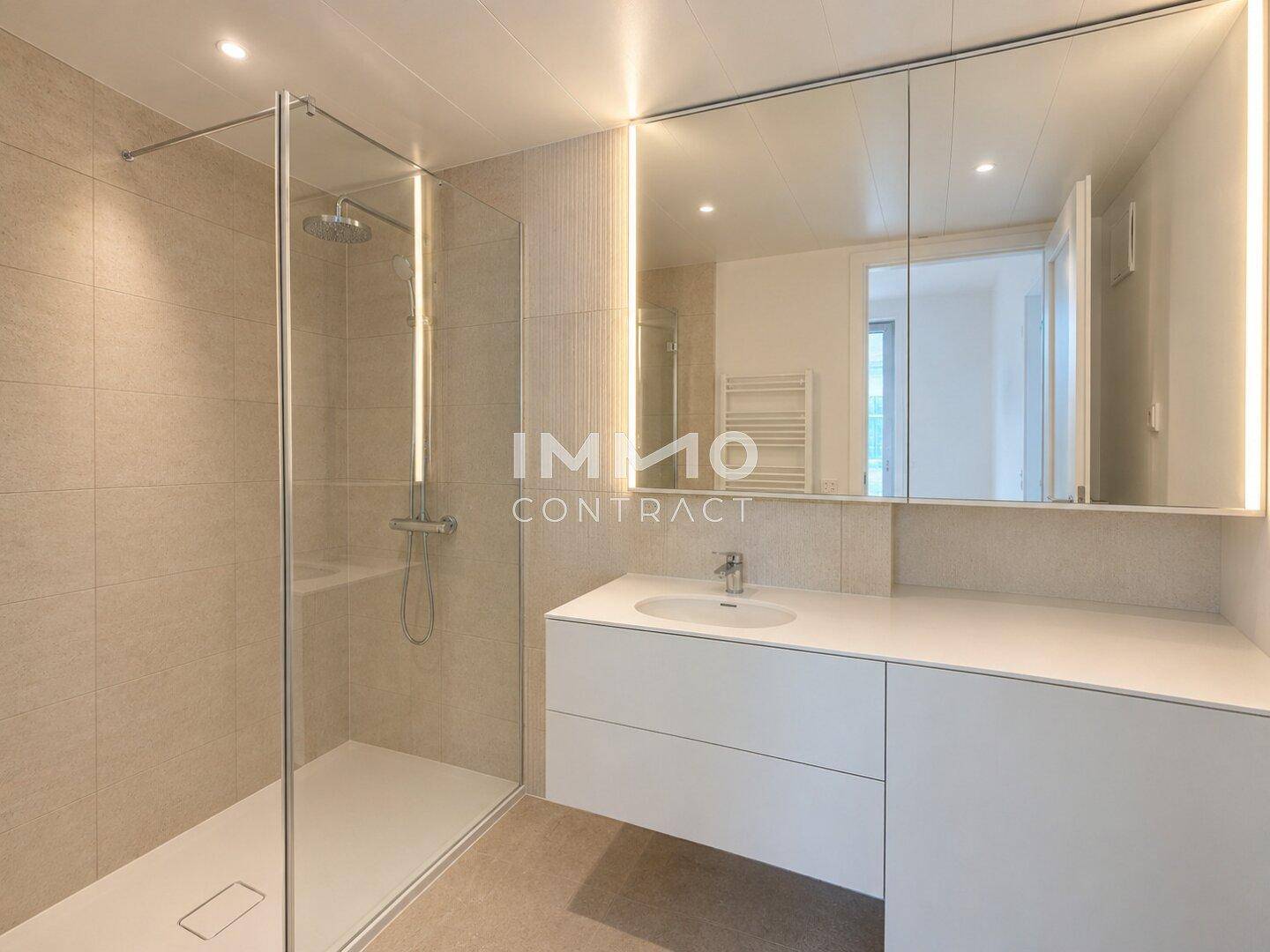 Modernes Badezimmer mit begehbarer Dusche, großem Spiegel und integrierter Beleuchtung.