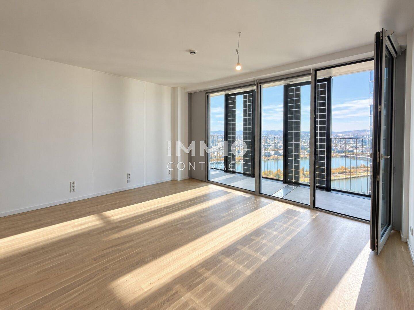 Geräumiges Wohnzimmer mit Holzboden, viel Tageslicht und Zugang zu einem Balkon mit Flussblick.