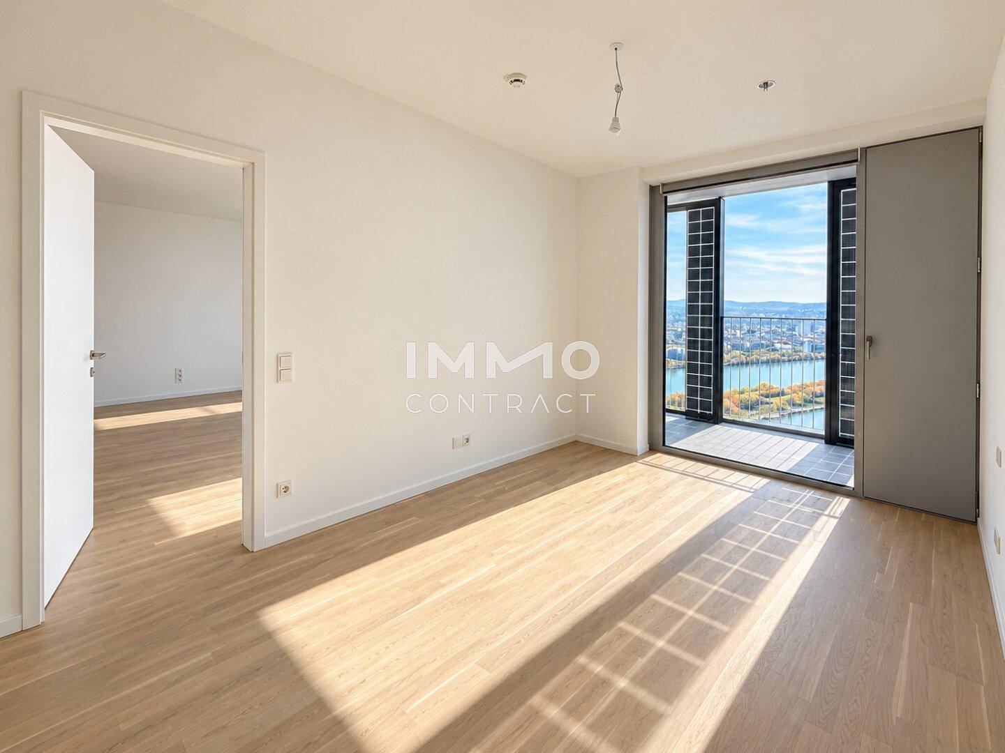 Heller Raum mit Holzboden und Zugang zu einem Balkon, der einen weiten Blick bietet.