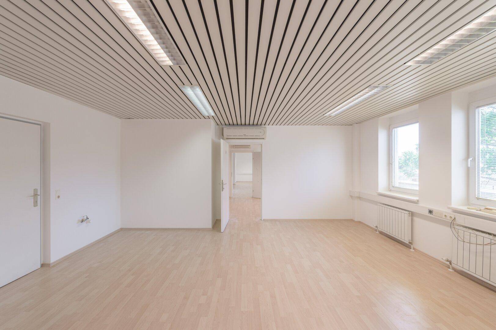 Großer, heller Büroraum mit Klimaanlage, Lamellendecke und Fenstern für viel Tageslicht.