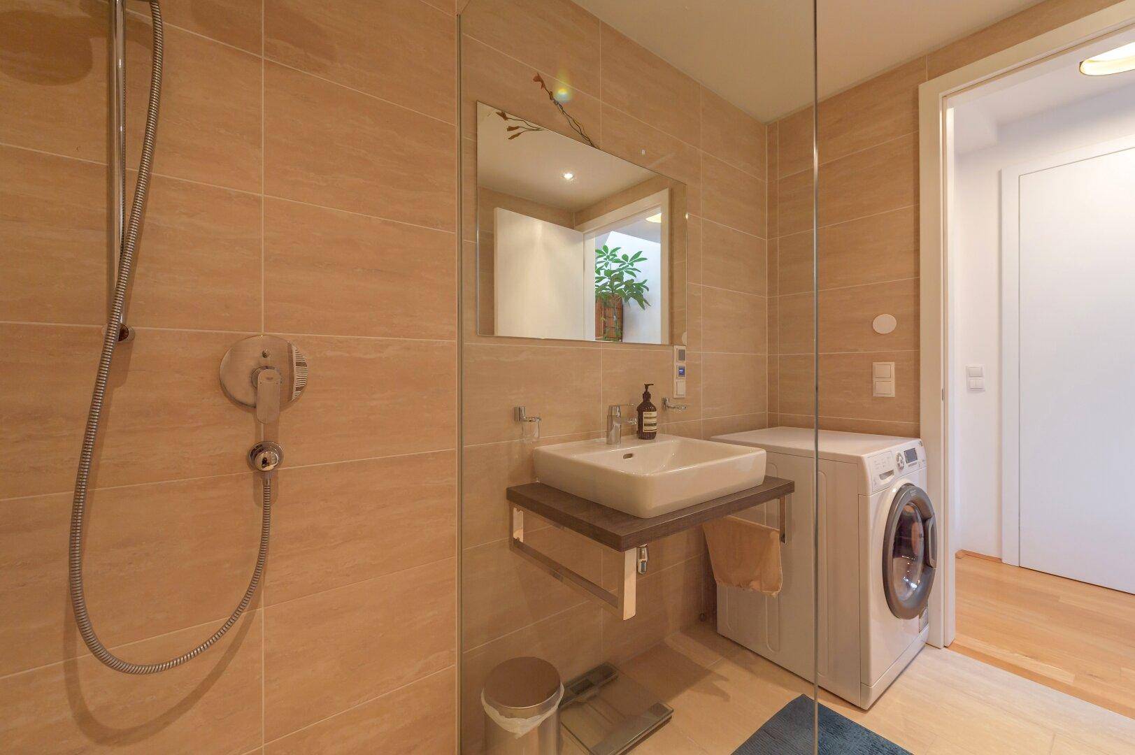 Modernes Badezimmer mit begehbarer Dusche, Waschbecken und integrierter Waschmaschine.