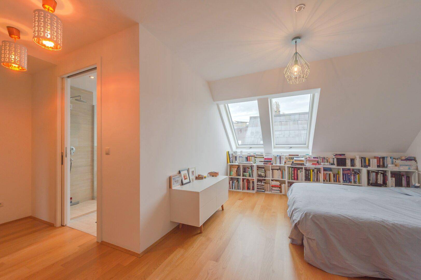Schlafzimmer im Dachgeschoss mit Dachfenstern und Zugang zu einem modernen Badezimmer.