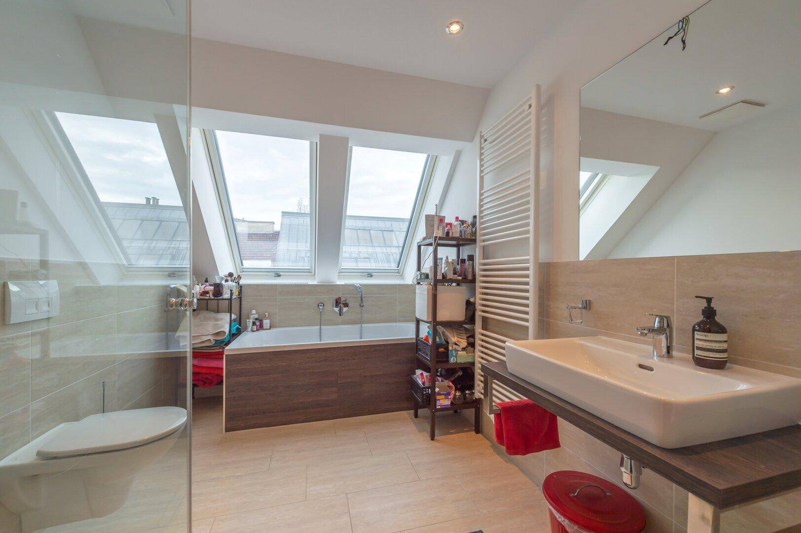Helles Badezimmer mit Badewanne, Waschbecken, Toilette und großen Dachfenstern.
