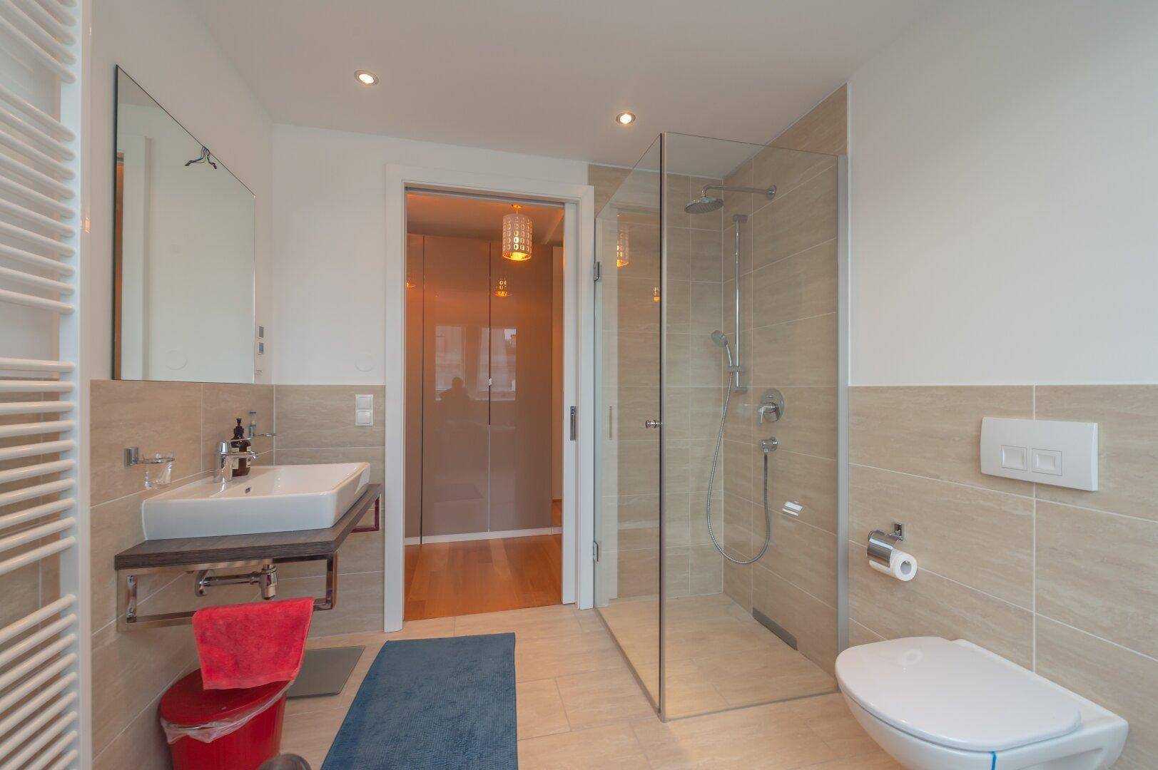 Modernes Badezimmer mit begehbarer Dusche, Waschbecken und Toilette in hellen Farbtönen.