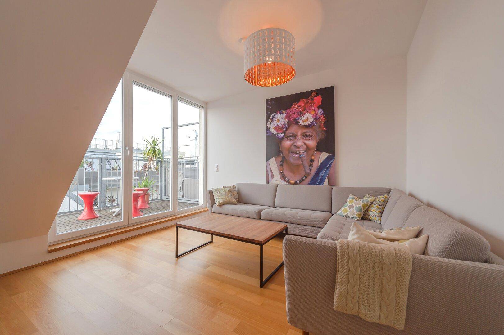 Geräumiges Wohnzimmer mit großem Sofa, Holzboden und Zugang zur Dachterrasse.