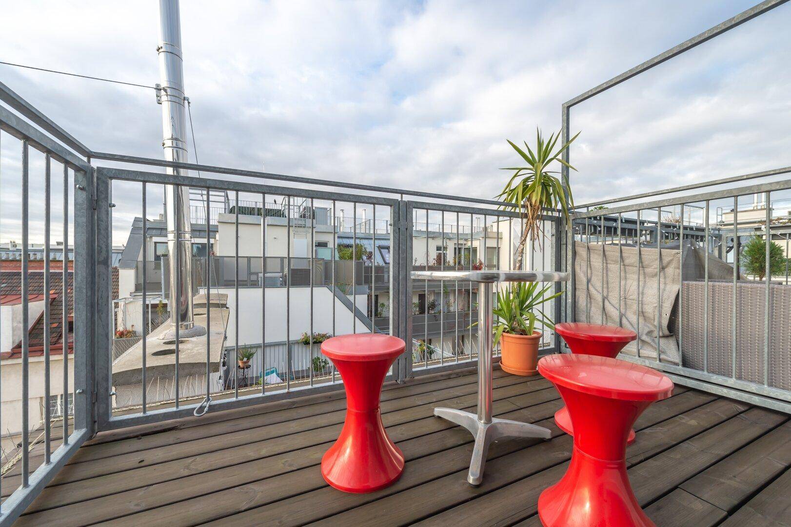 Dachterrasse mit Metallgeländer, Sitzgelegenheiten und Blick über die umliegenden Dächer.