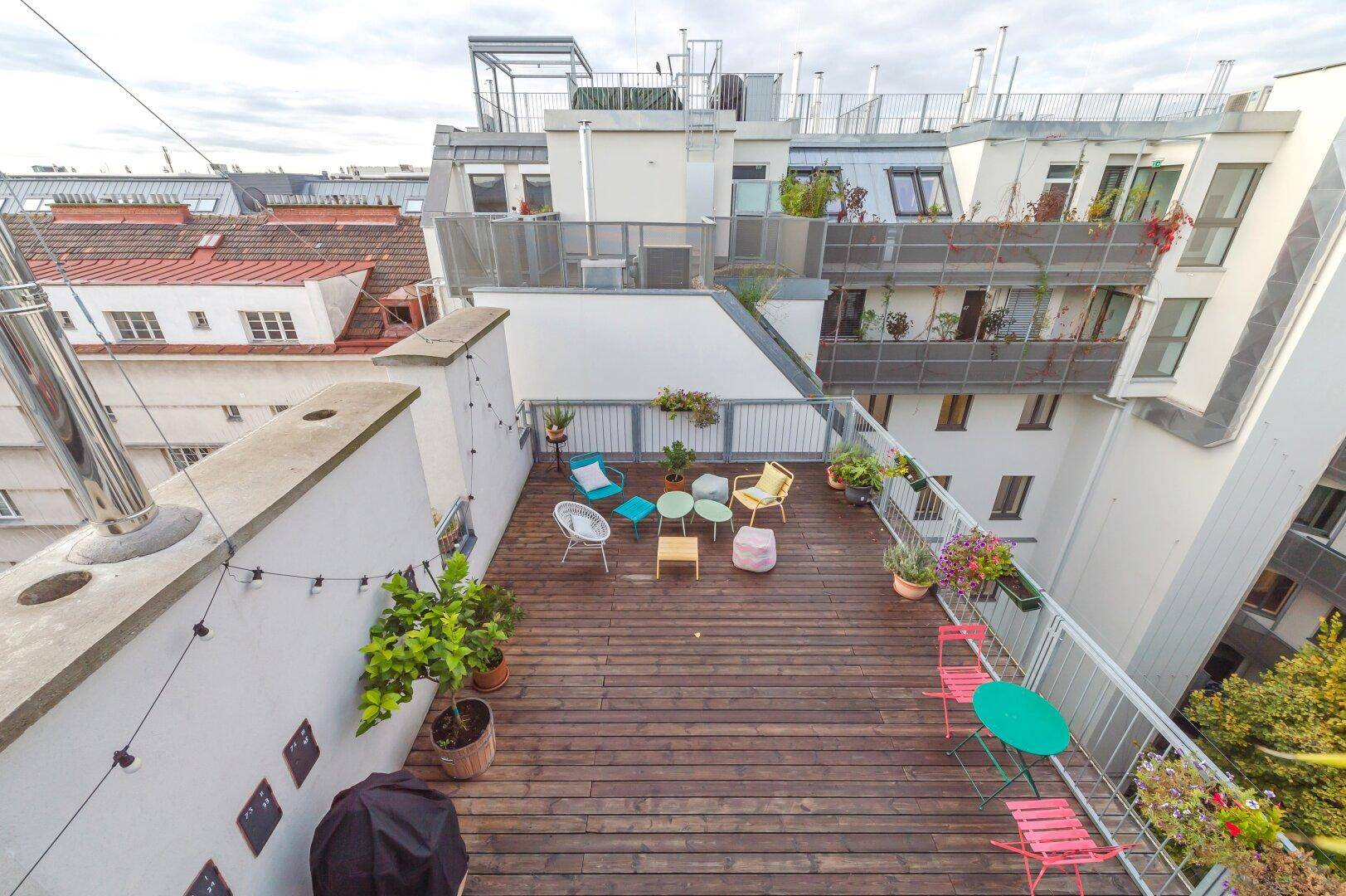 Große Dachterrasse mit Holzboden, Pflanzen und vielfältigen Sitzmöglichkeiten.