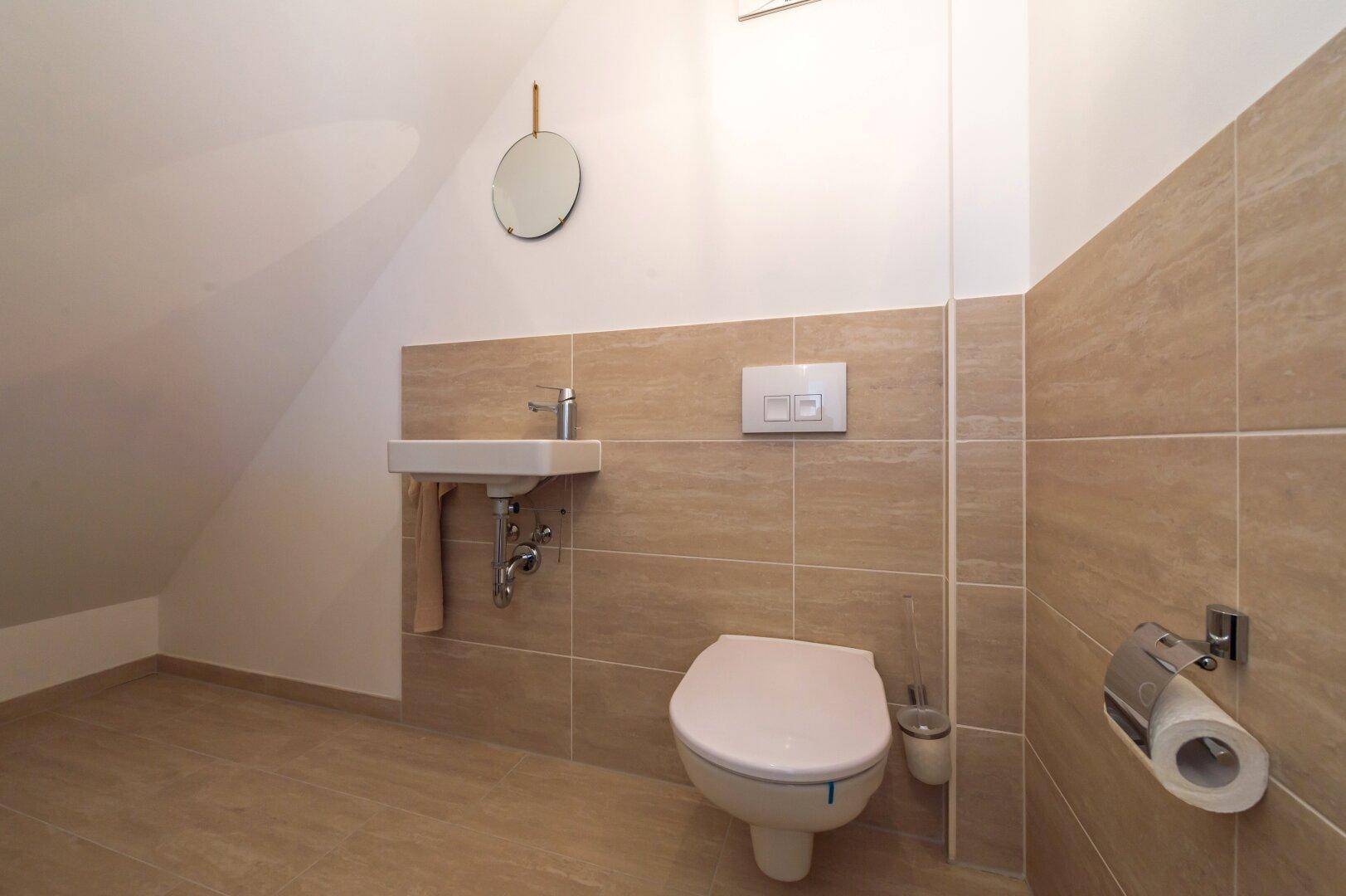 Modernes Gäste-WC mit beigefarbenen Fliesen, wandhängendem WC und kleinem Waschbecken.