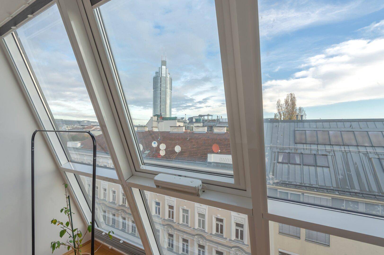 Weitblick über die Dächer der Stadt mit modernem Hochhaus durch große Dachfenster.