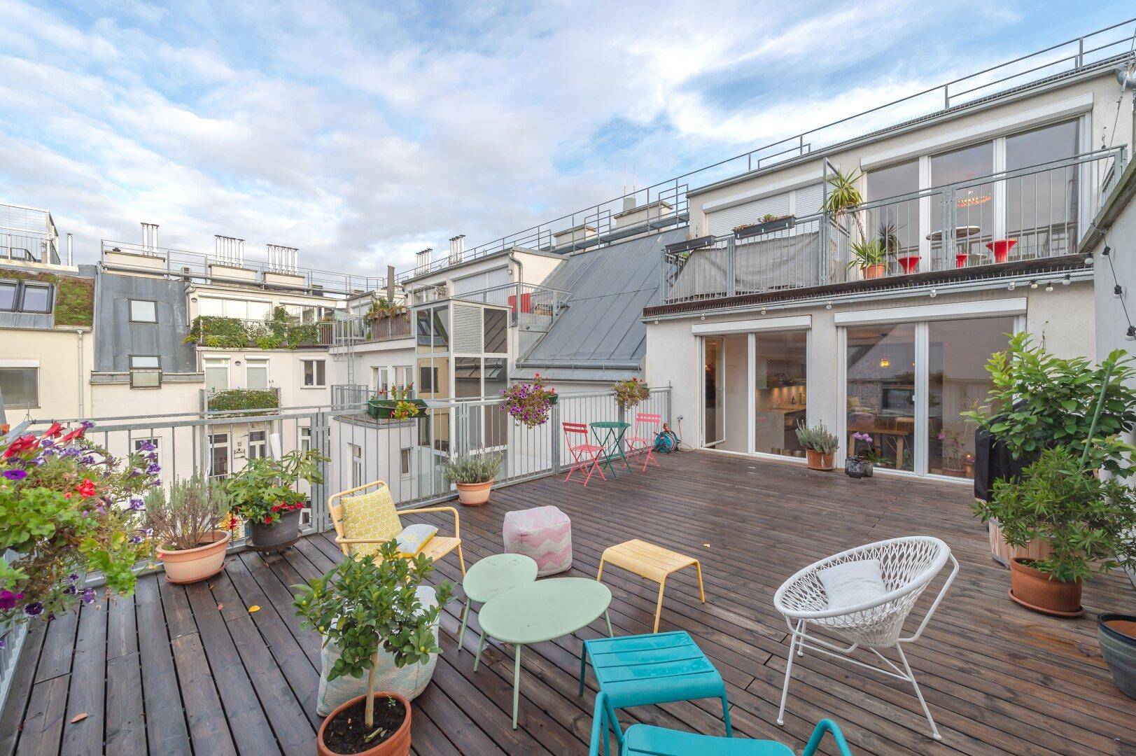 Weitläufige Dachterrasse mit Holzboden, bunten Möbeln und vielen Pflanzen.