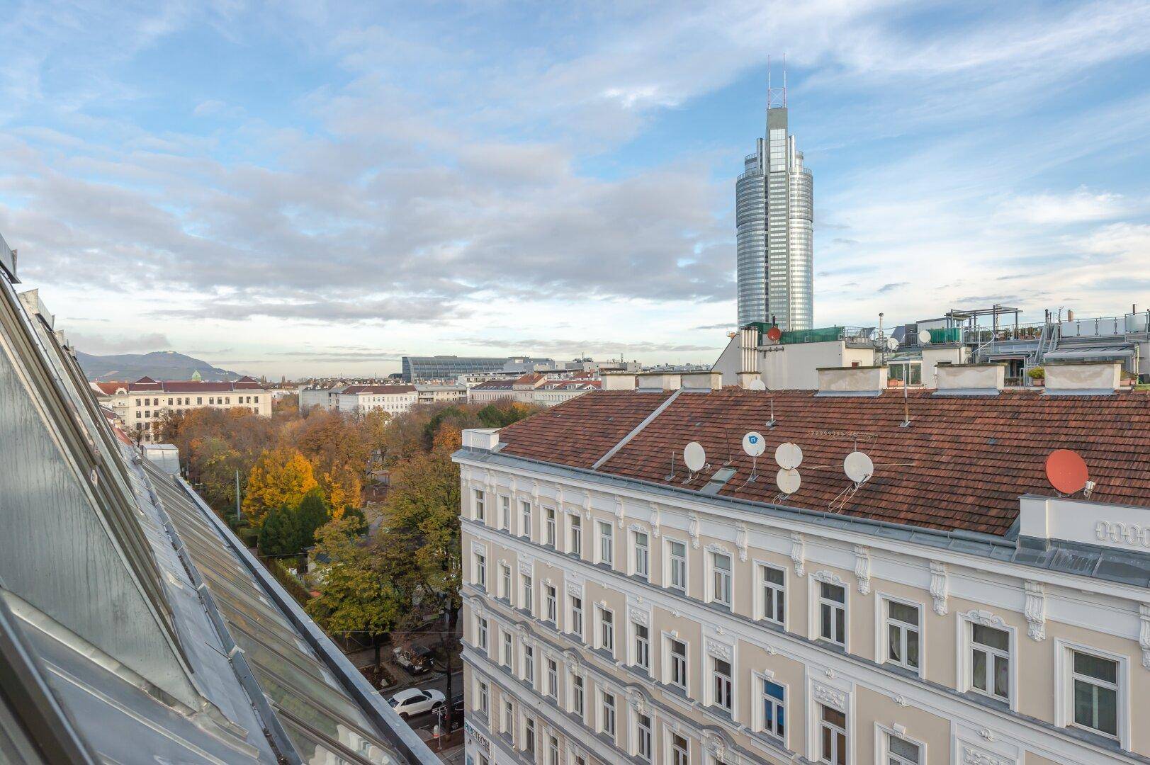 Panoramablick über die Stadt mit Herbstbäumen und einem markanten Hochhaus am Horizont.