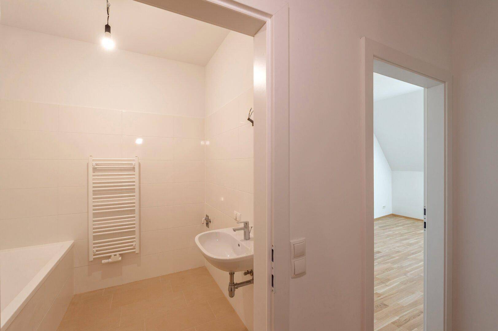 Modernes Badezimmer mit Badewanne, beheiztem Handtuchhalter und hellen Fliesen.