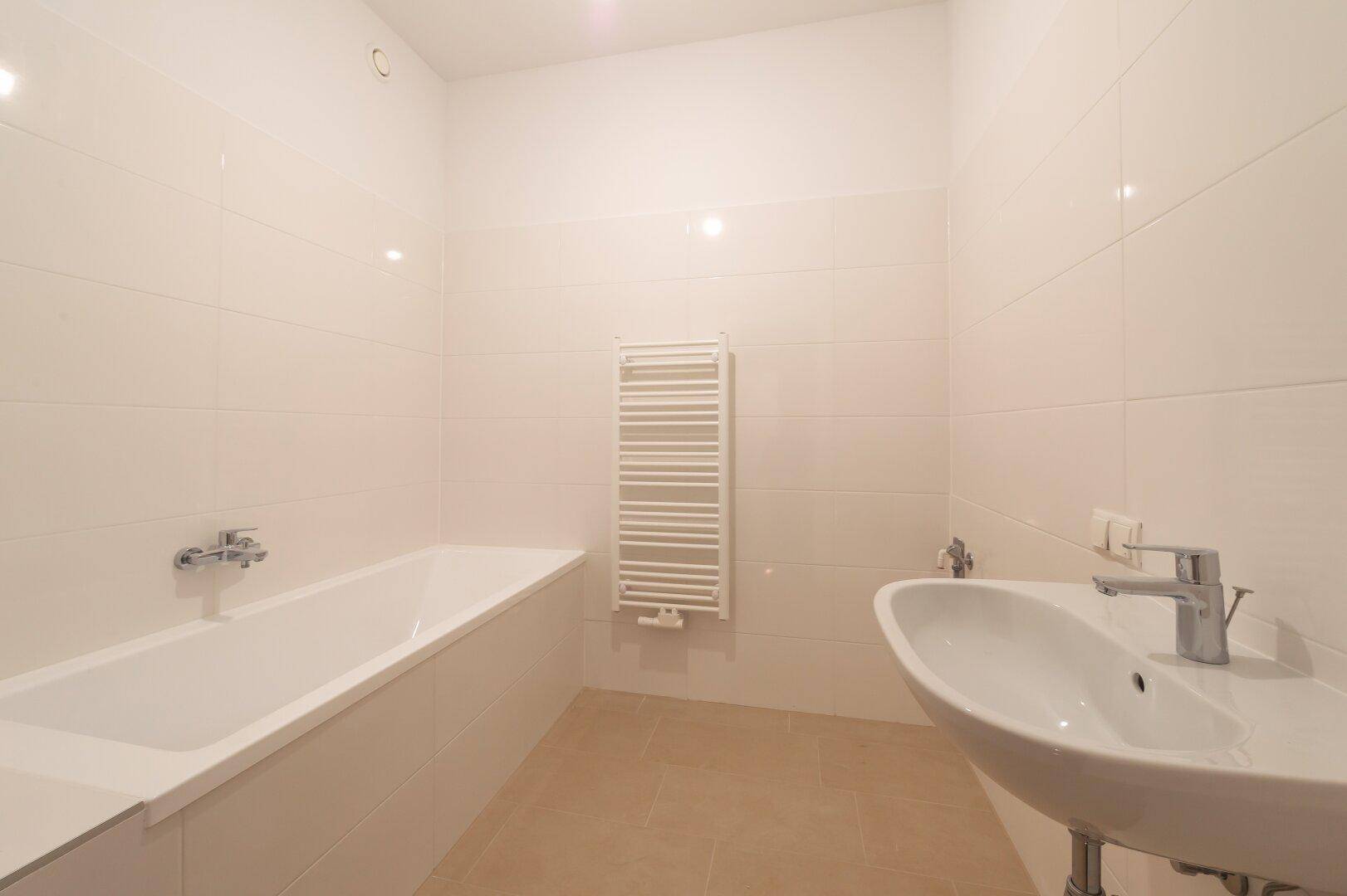 Helles Badezimmer mit Badewanne, Waschbecken und praktischem Handtuchheizkörper.