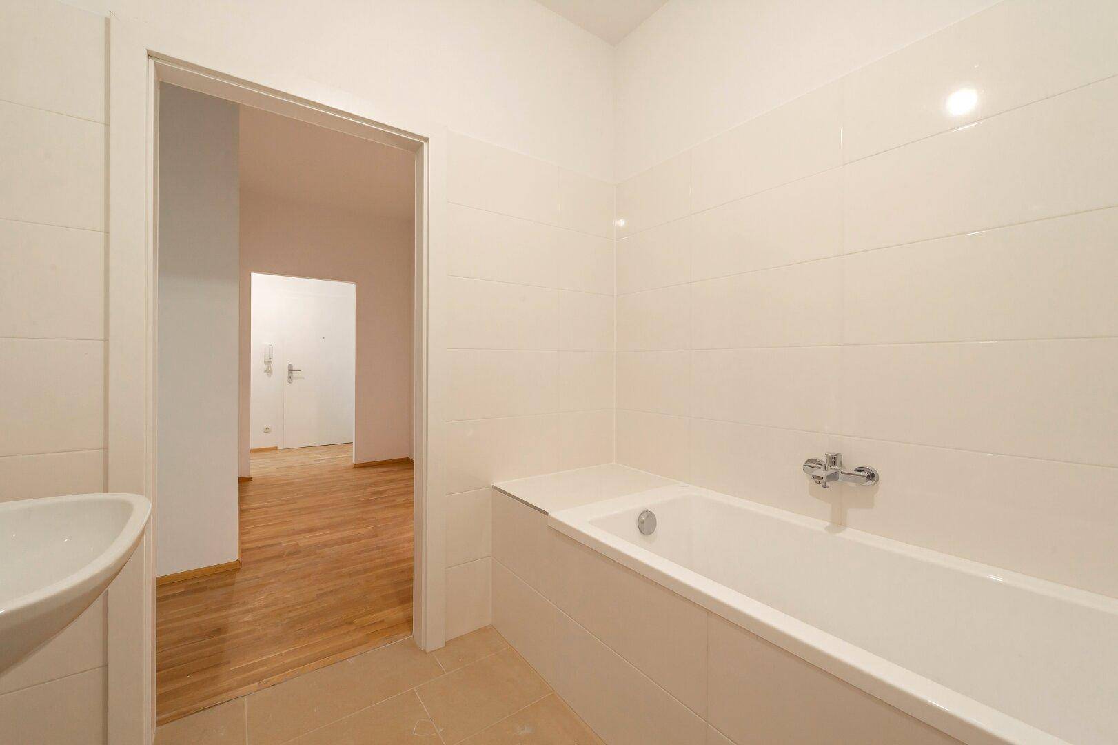 Modernes Badezimmer mit Badewanne und Waschbecken, durch eine Tür mit dem Flur verbunden.