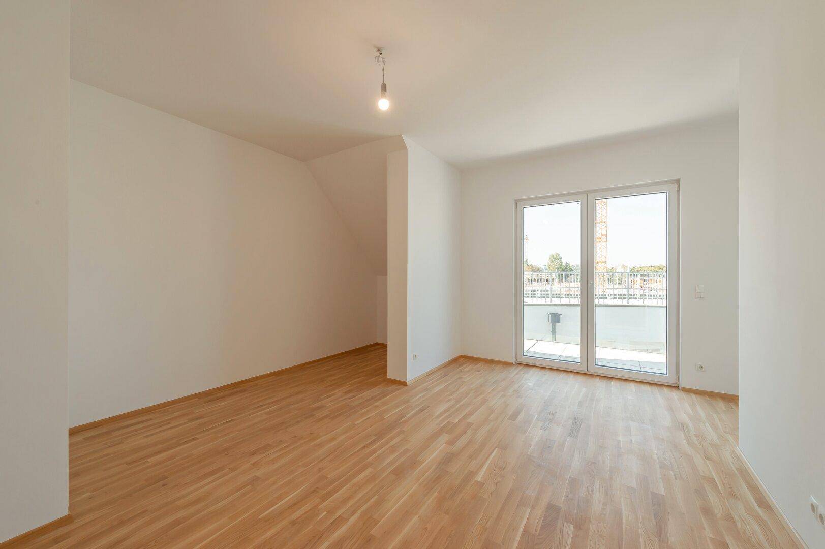 Helles Zimmer mit Holzboden und großen Fenstern, die Zugang zu einem Außenbereich bieten.