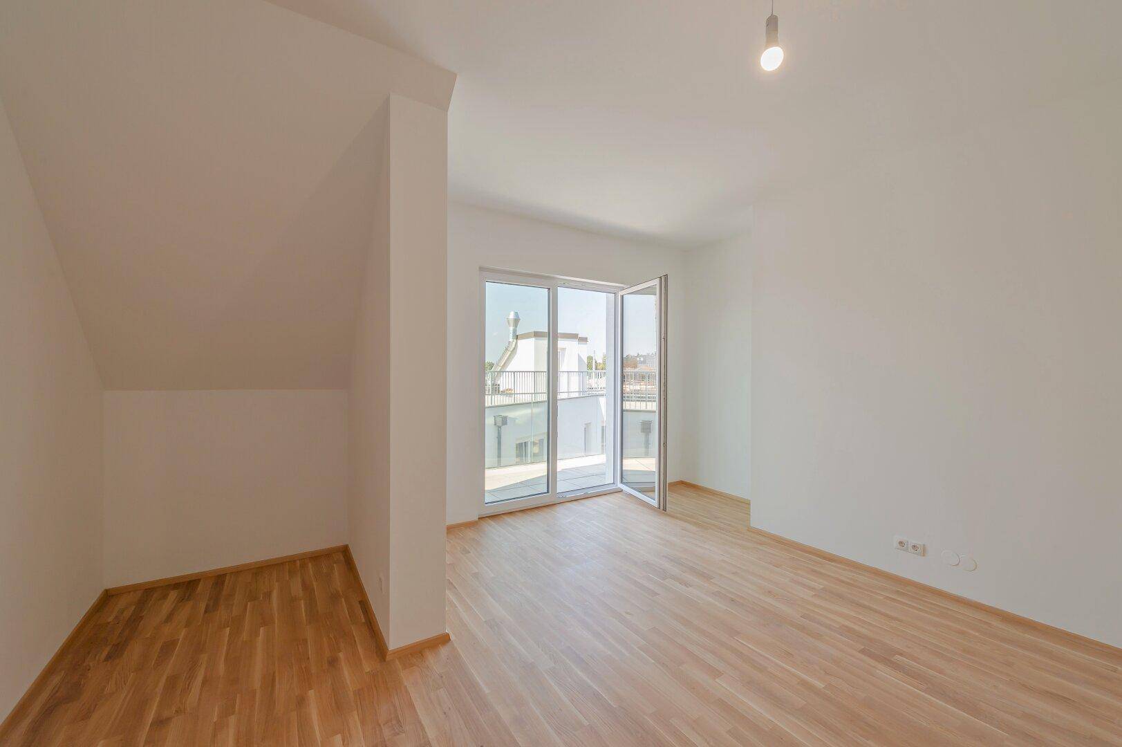 Geräumiges Zimmer mit Holzboden und großen Glastüren, die auf einen Balkon führen.