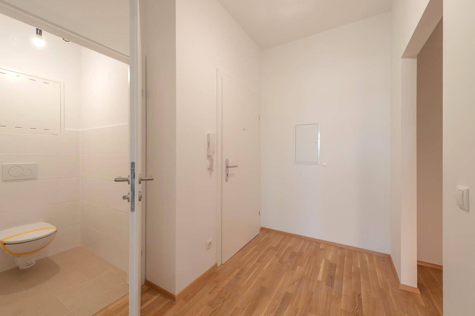 Heller Flur mit Holzboden und Zugang zu einem Gäste-WC, ausgestattet mit weißen Fliesen.