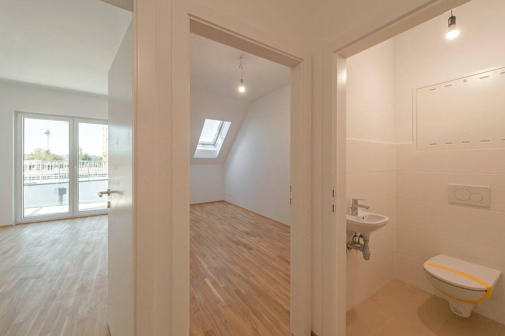 Heller Flur mit Holzboden, der zu einem Zimmer mit Dachfenster und einem Gäste-WC führt.