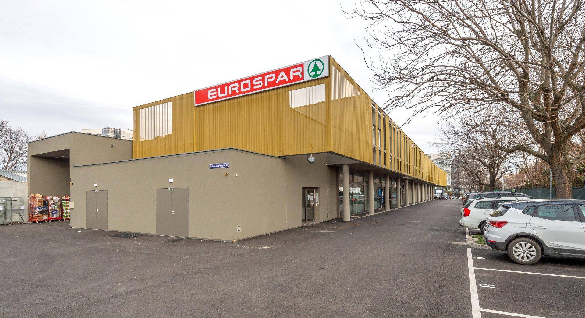 Außenansicht eines Eurospar-Supermarktes mit großem Parkplatz und umliegenden Bäumen.